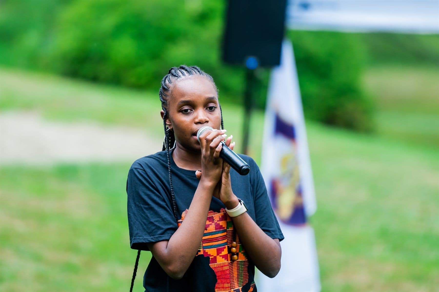 A young camper singing beside the flags, wearing a shirt printed with the map of Africa