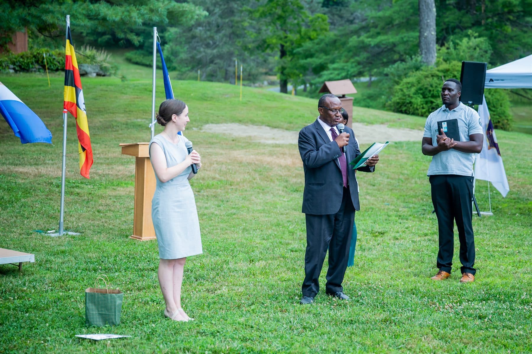 Speakers delivering welcome addresses at an outdoor podium beside the flags