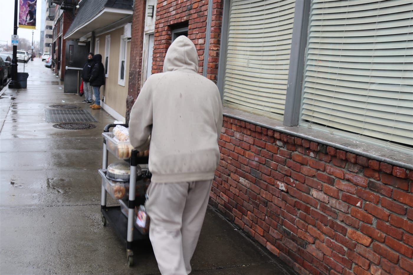 A volunteer pushing a cart of food along a brick building